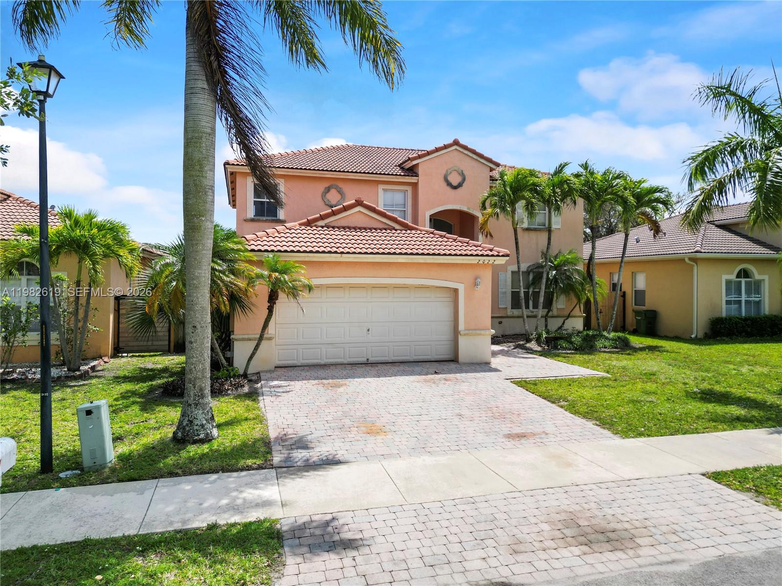 A two-story peach-colored house features a tiled roof, a two-car garage, and palm trees — 2022 SE 18th St, Homestead FL 33035, HOMESTEAD, FL