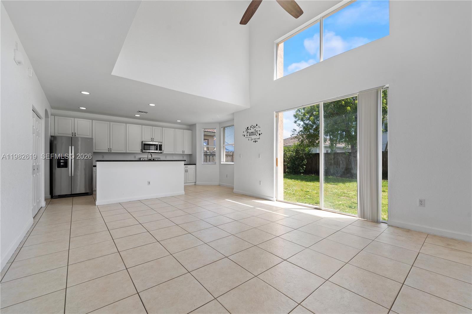 A kitchen with white cabinets and stainless appliances opens to a living area with tile — 2022 SE 18th St, Homestead FL 33035, HOMESTEAD, FL