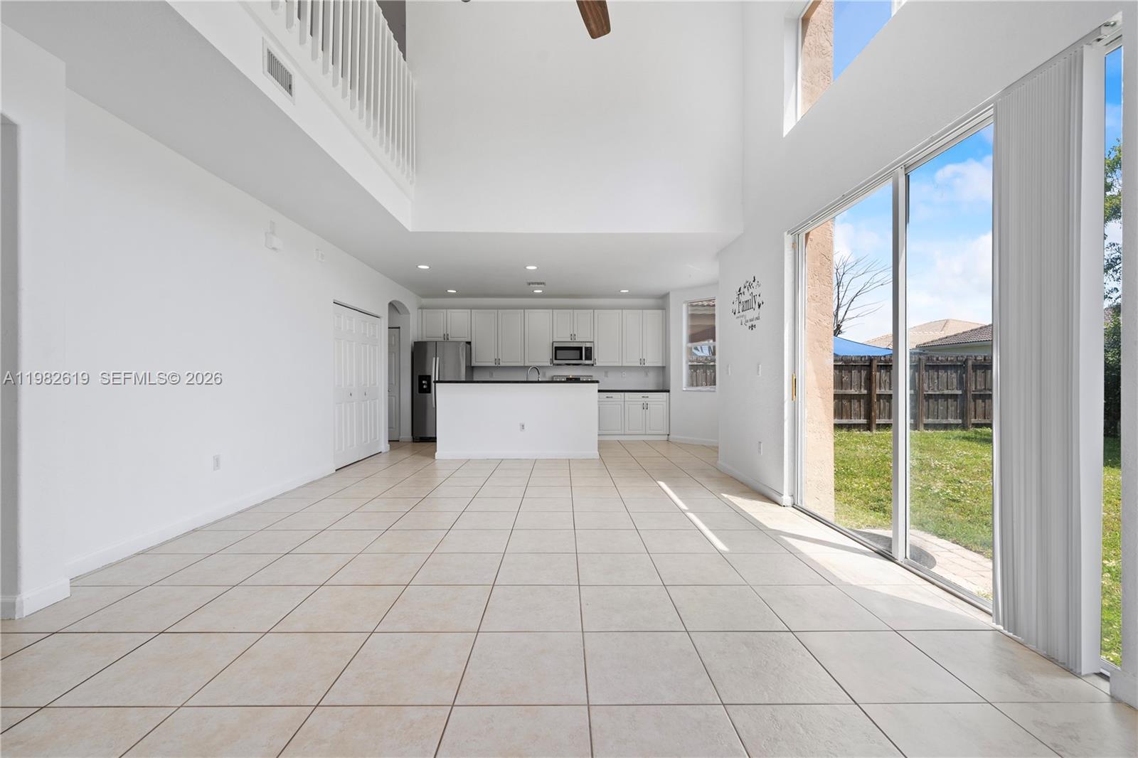 A bright, open-concept kitchen and living area features white cabinetry, tile flooring, and high ceilings — 2022 SE 18th St, Homestead FL 33035, HOMESTEAD, FL