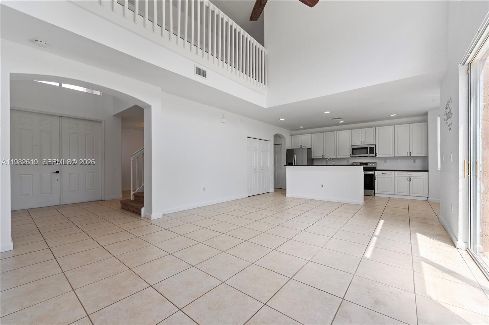 An open-concept living area features a kitchen with white cabinets and tile flooring — 2022 SE 18th St, Homestead FL 33035, HOMESTEAD, FL