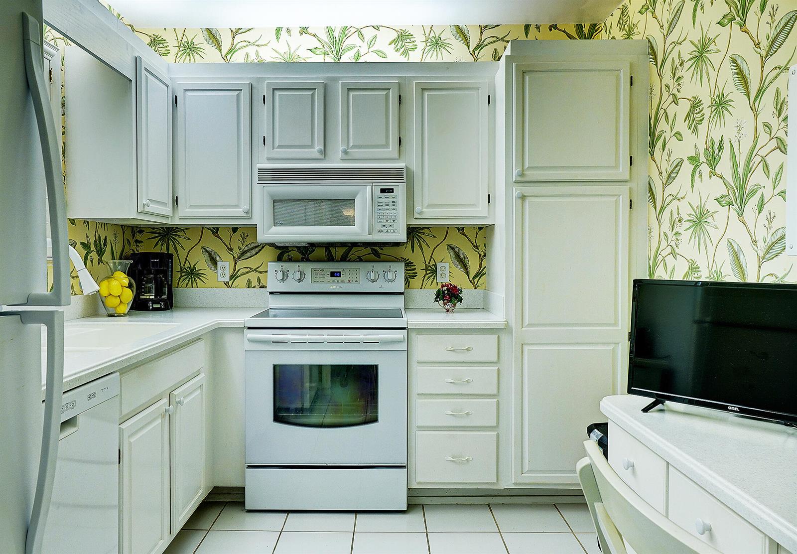 A kitchen with white cabinets, a white stove, and wallpaper featuring a green palm pattern — 2370 NE Ocean Boulevard # C305, Stuart FL 34996, STUART, FL
