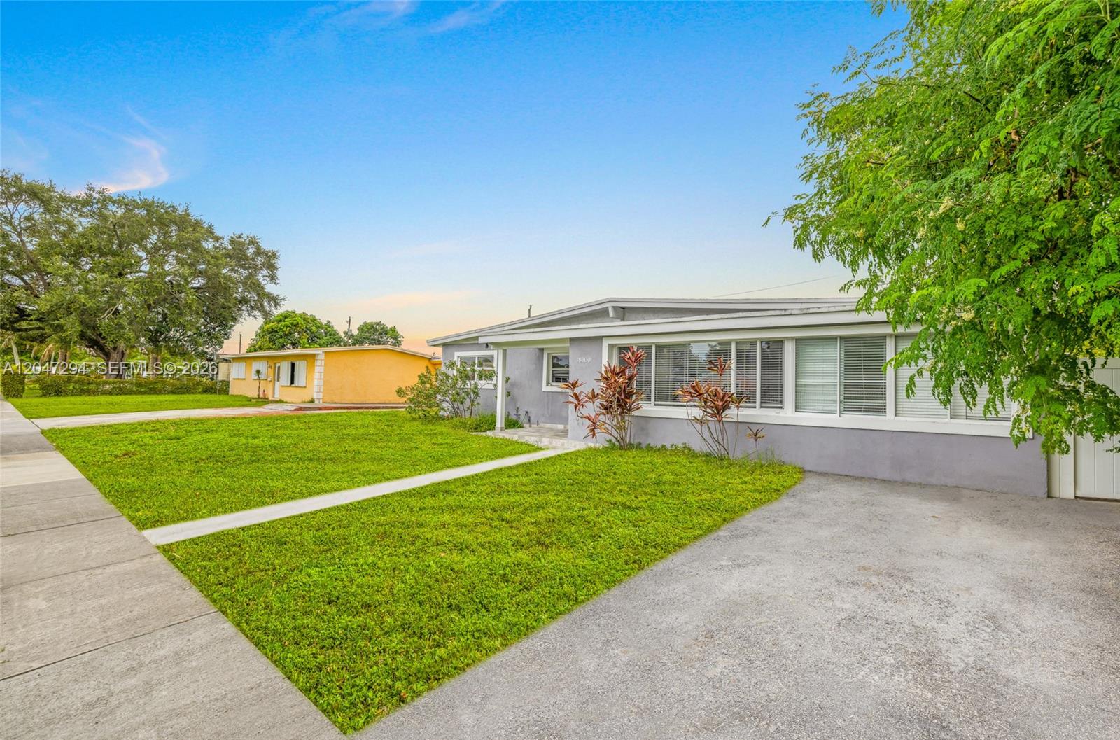 A gray single-story house with a concrete driveway and a front lawn under a blue sky — 18100 NW 7th Pl, Miami Gardens FL 33169, MIAMI GARDENS, FL