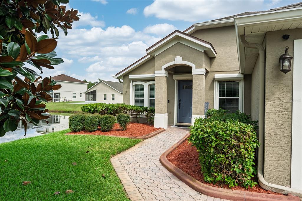 A paved walkway leads to the front entrance of a tan house with a blue door — 14001 FAIRWINDS COURT, ORLANDO, FL