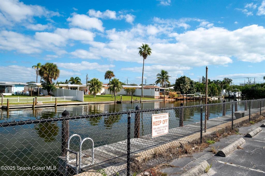 A chain-link fence separates a paved parking area from a canal with private docks — 333 W COCOA BEACH CAUSEWAY UNIT 5, COCOA BEACH, FL