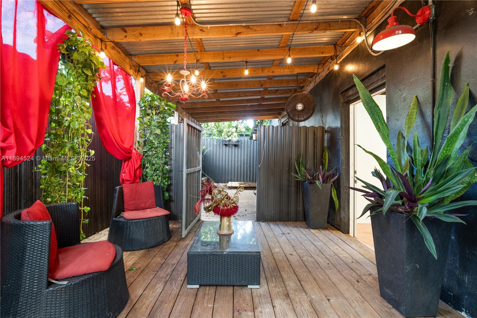 A covered outdoor patio features wooden decking, wicker furniture with red cushions, and string lights — 2900 NW 11th Ave, Miami FL 33127, MIAMI, FL