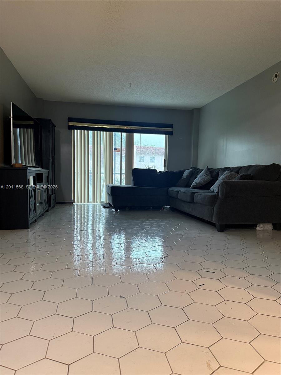 A living room features a dark sectional sofa, a television console, and white hexagonal floor tiles — 4176 Inverrary Dr # 103, Lauderhill FL 33319, LAUDERHILL, FL