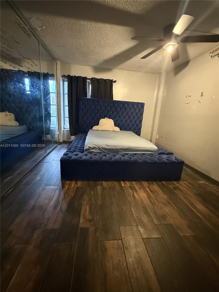 A bedroom features a large blue tufted platform bed, dark wood flooring, and mirrored closets — 4176 Inverrary Dr # 103, Lauderhill FL 33319, LAUDERHILL, FL
