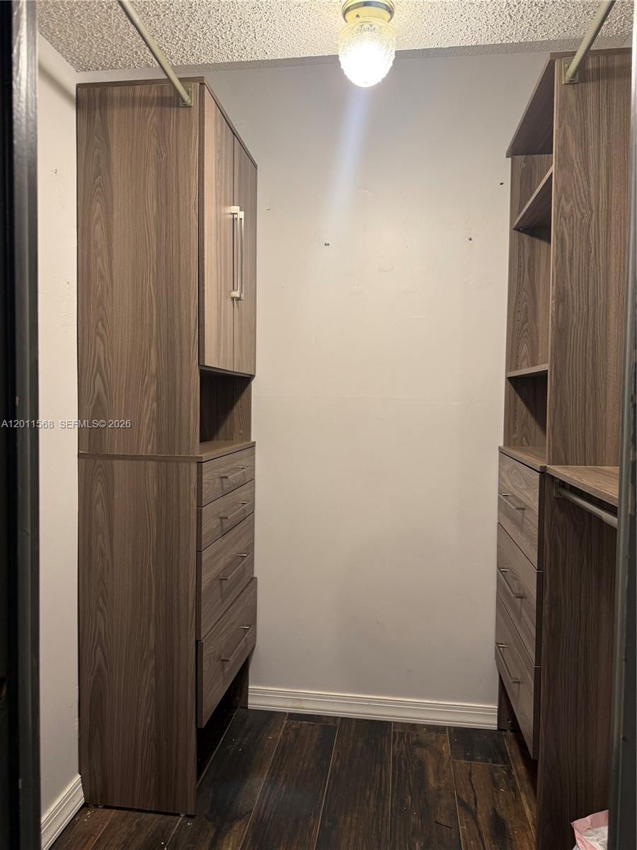 A walk-in closet features wood-grain storage units with drawers, shelving, and hanging rods — 4176 Inverrary Dr # 103, Lauderhill FL 33319, LAUDERHILL, FL