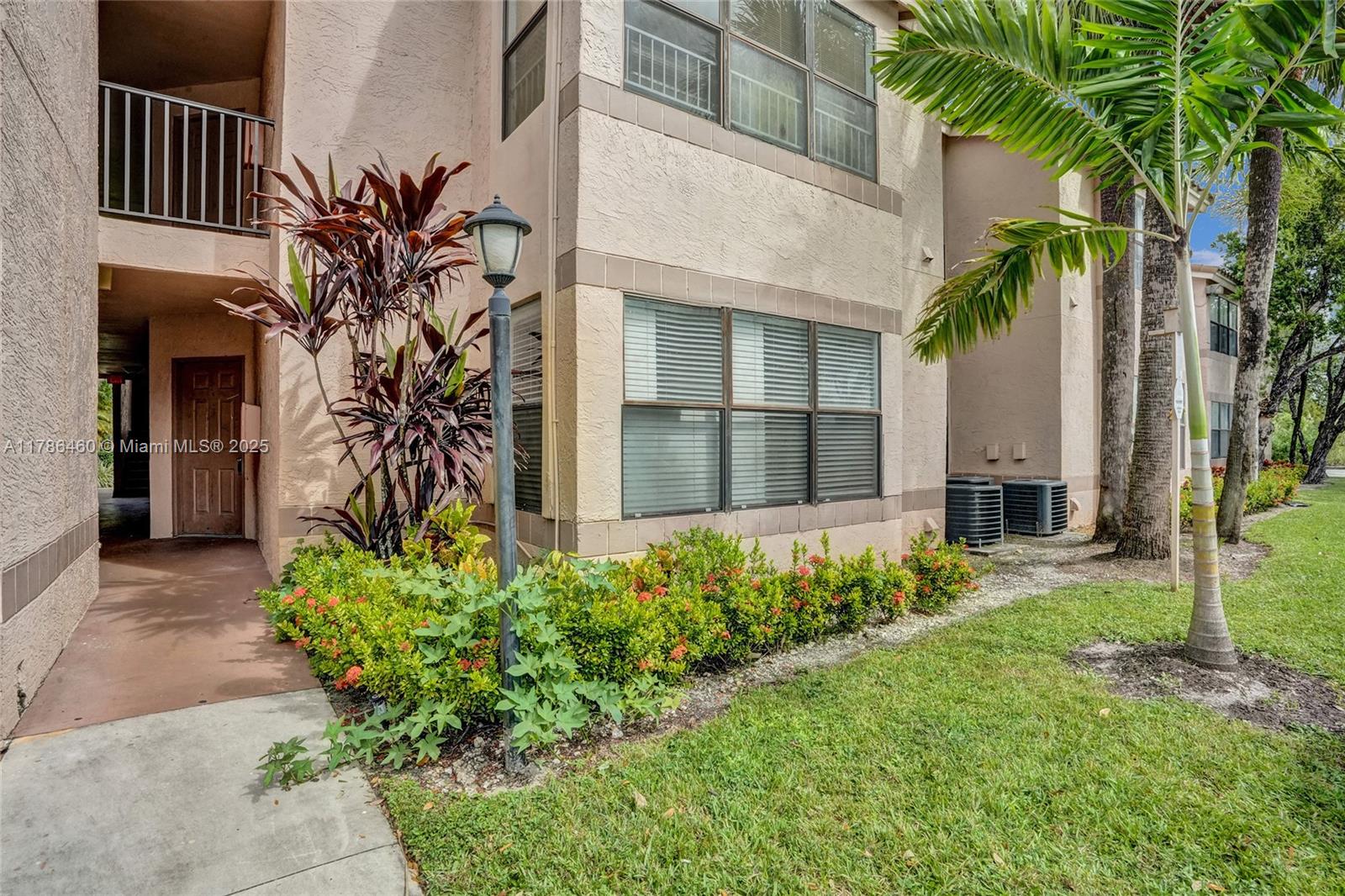 The exterior of a multi-story stucco apartment building features a walkway, landscaping, and palm trees — 2946 S University Dr # 7108, Davie FL 33328, DAVIE, FL