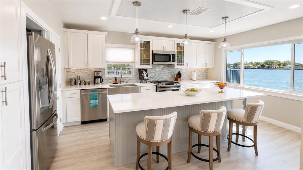 A bright kitchen features white cabinets, a central island with bar stools, and water views — 526 20TH AVENUE, INDIAN ROCKS BEACH, FL