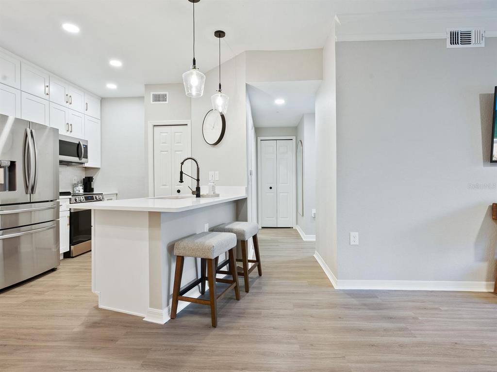 A modern kitchen features white cabinets, stainless steel appliances, a breakfast bar, and wood flooring — 5168 NORTHRIDGE ROAD UNIT 102, SARASOTA, FL