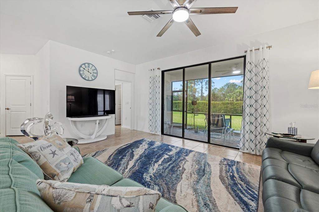 A living room features a blue patterned rug, a ceiling fan, and sliding glass doors — 2081 GARDENIA AVENUE, PORT CHARLOTTE, FL