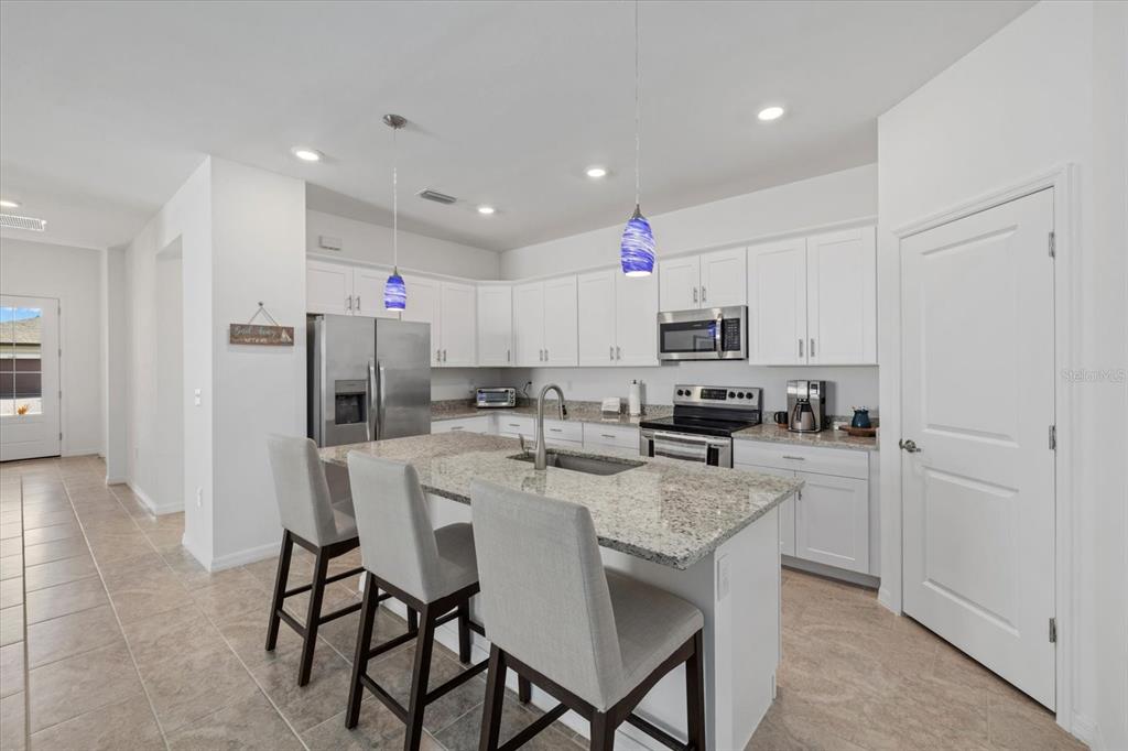 A kitchen features white cabinets, granite countertops, a center island with seating, and stainless appliances — 2081 GARDENIA AVENUE, PORT CHARLOTTE, FL