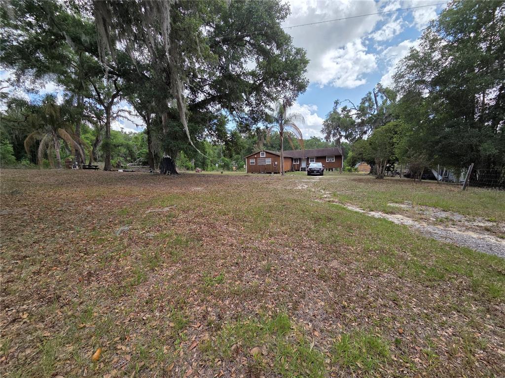 A brown single-story house sits on a large, grassy lot with many mature trees — 27440 WINCHESTER DRIVE, BROOKSVILLE, FL
