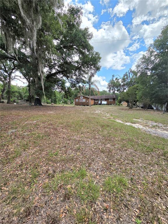 A brown single-story house sits on a large, grassy lot with mature trees — 27440 WINCHESTER DRIVE, BROOKSVILLE, FL
