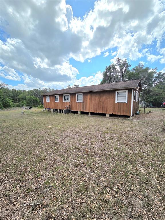 A long, single-story mobile home with wood siding sits on a grassy lot — 27440 WINCHESTER DRIVE, BROOKSVILLE, FL