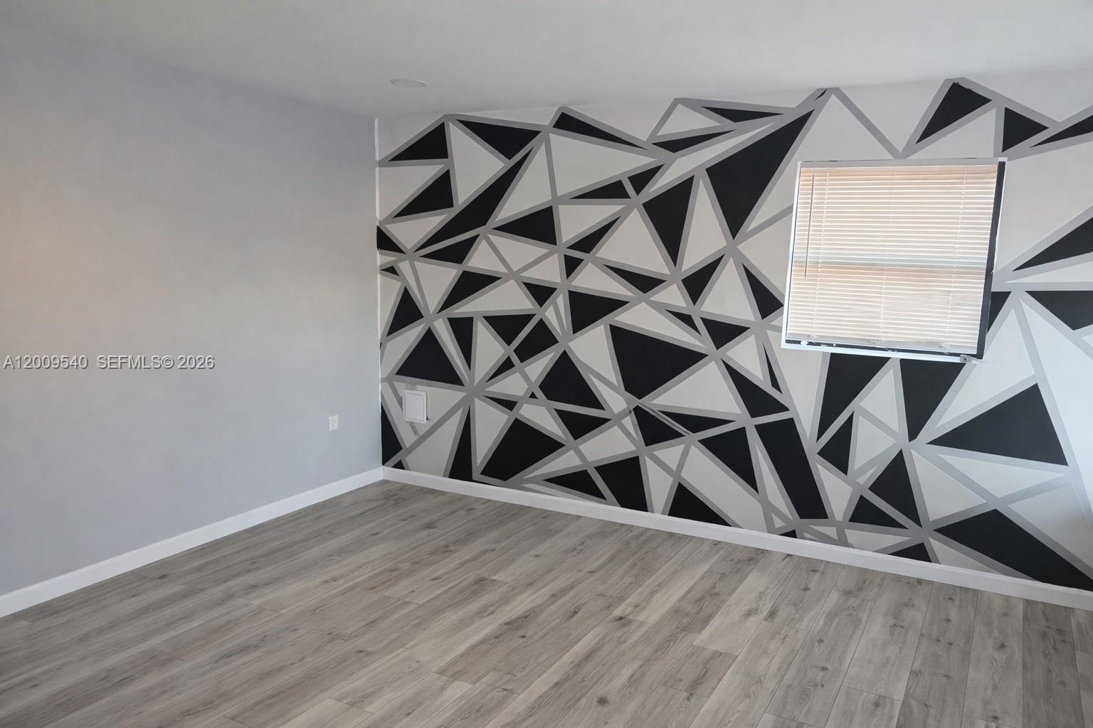 An empty room features light wood-look flooring and an accent wall with a geometric pattern — 1822 N Dixie Hwy, Hollywood FL 33020, HOLLYWOOD, FL