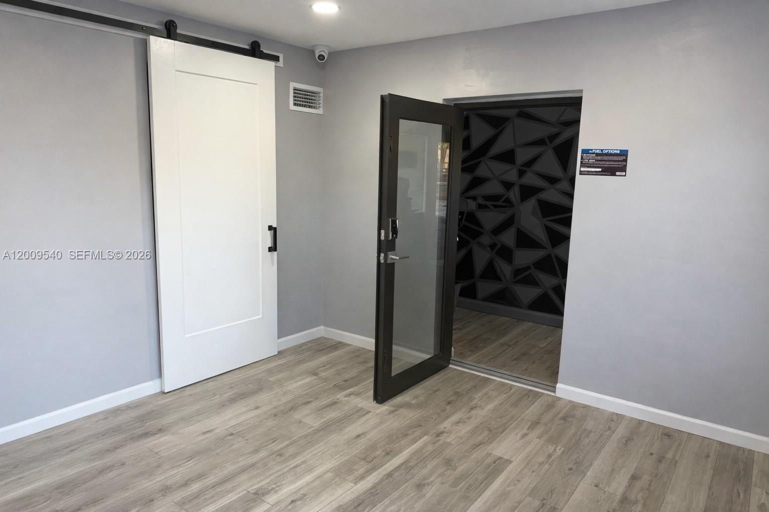 A room with light wood-look flooring, a white barn door, and an open glass door — 1822 N Dixie Hwy, Hollywood FL 33020, HOLLYWOOD, FL