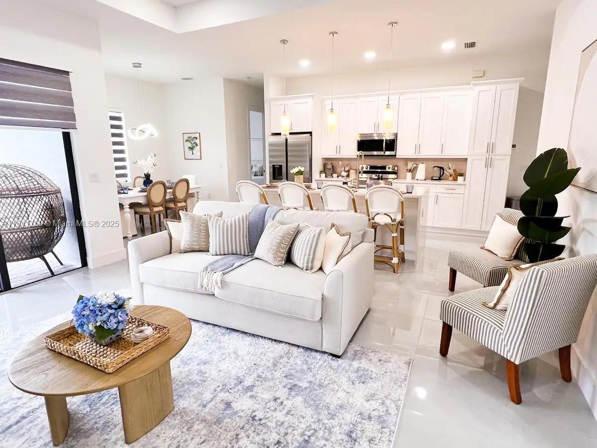 A bright, open-concept living room and kitchen feature white cabinetry, tile floors, and neutral furniture — 404 NW 1st ST, Cape Coral FL 33993, CAPE CORAL, FL