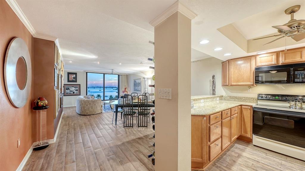 A kitchen with wood cabinets and granite countertops overlooks a dining area with water views — 707 S GULFSTREAM AVENUE UNIT 705, SARASOTA, FL