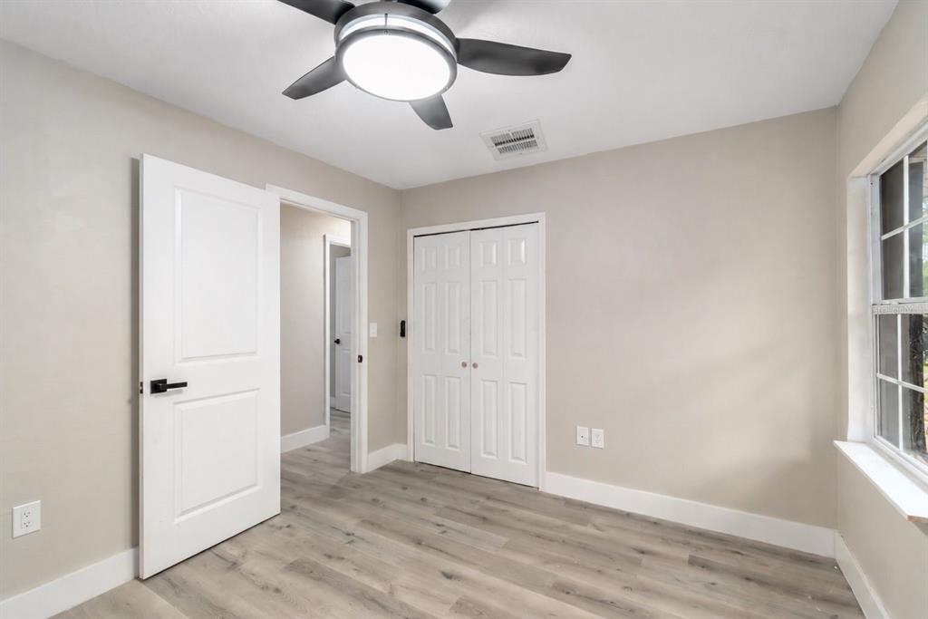 A bedroom with light gray walls, wood-look flooring, a ceiling fan, and white closet doors — 1702 NW 27TH AVENUE, OCALA, FL