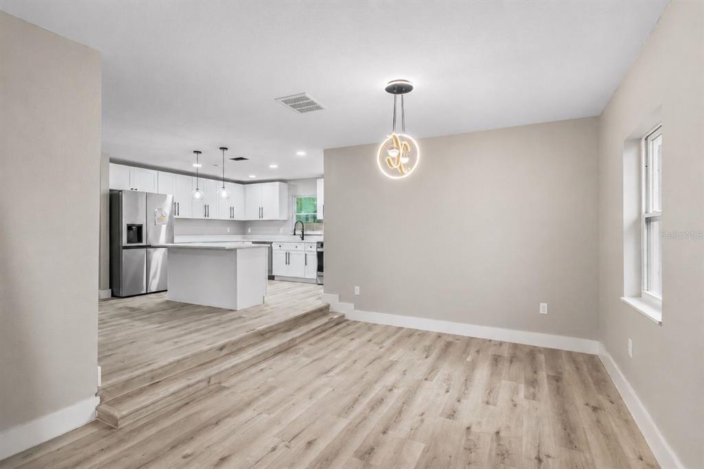A kitchen with white cabinets and an island overlooks a dining area with wood-look flooring — 1702 NW 27TH AVENUE, OCALA, FL