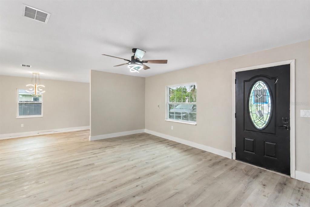 A living room with light wood-look flooring, a ceiling fan, and a black front door — 1702 NW 27TH AVENUE, OCALA, FL