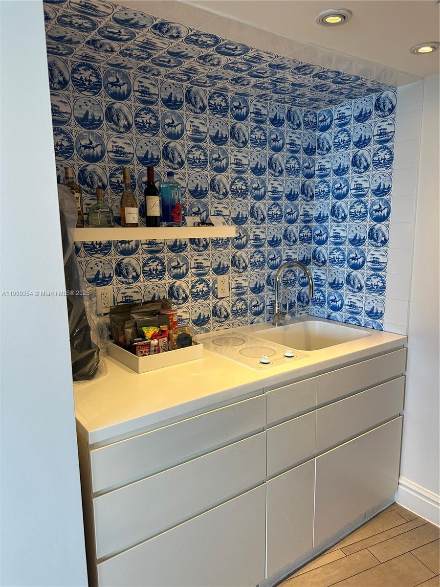 A small kitchenette features white cabinets, a sink, a cooktop, and blue patterned tile walls — 1100 West Ave # 1206, Miami Beach FL 33139, MIAMI BEACH, FL