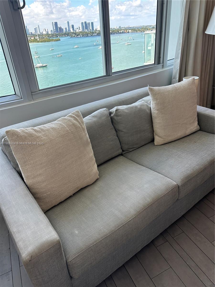 A gray sofa sits in front of a large window overlooking a bay and city — 1100 West Ave # 1206, Miami Beach FL 33139, MIAMI BEACH, FL