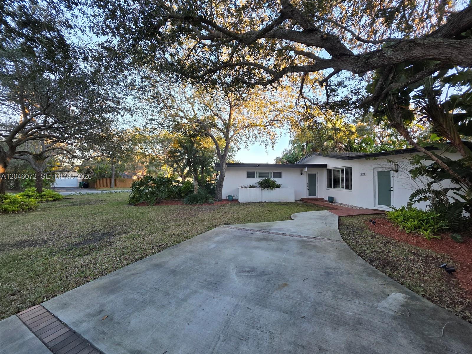 A white single-story house with a concrete driveway and large trees in the front yard — 9860 SW 140th St, Miami FL 33176, MIAMI, FL
