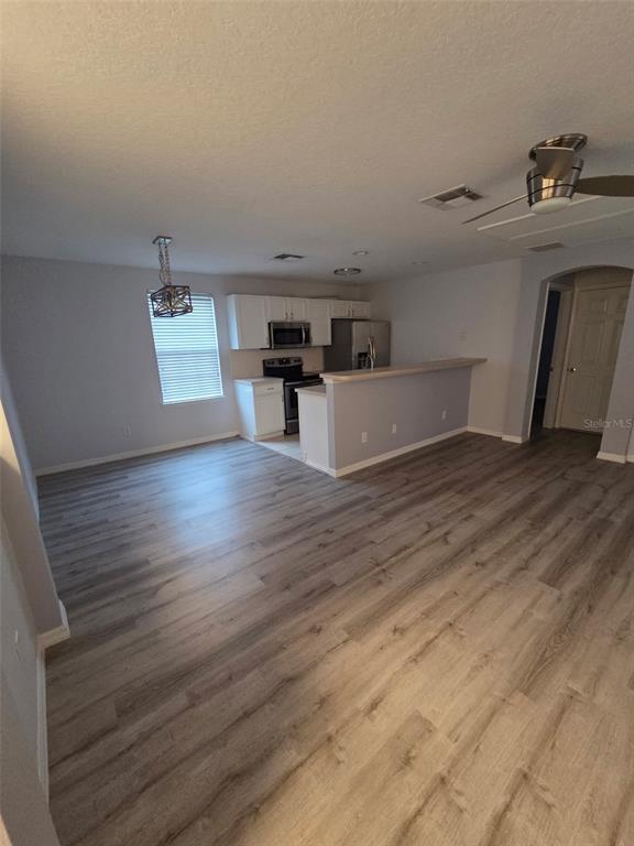An open-concept kitchen features white cabinetry, stainless steel appliances, and light wood-look flooring — 930 SPRING PARK LOOP UNIT B, KISSIMMEE, FL