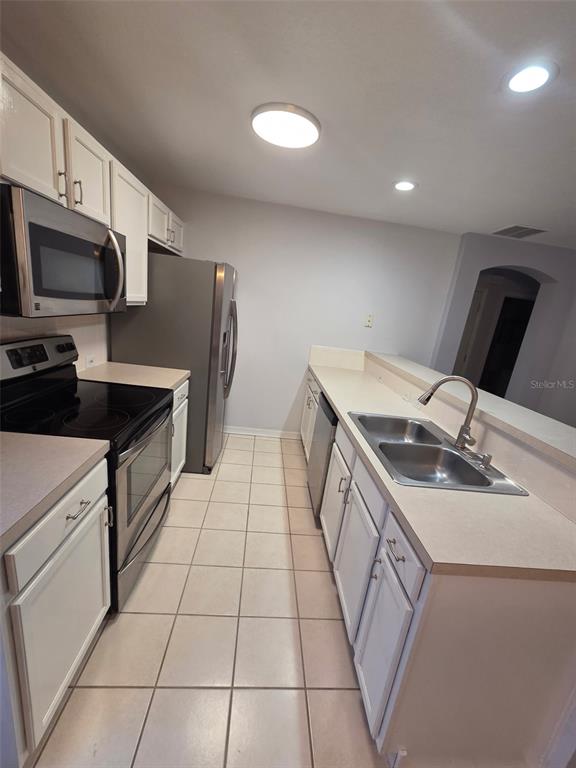 A galley kitchen features white cabinets, stainless steel appliances, and light-colored countertops — 930 SPRING PARK LOOP UNIT B, KISSIMMEE, FL