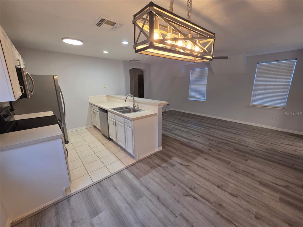 A kitchen with white cabinets and tile flooring opens into a living area with wood-look floors — 930 SPRING PARK LOOP UNIT B, KISSIMMEE, FL