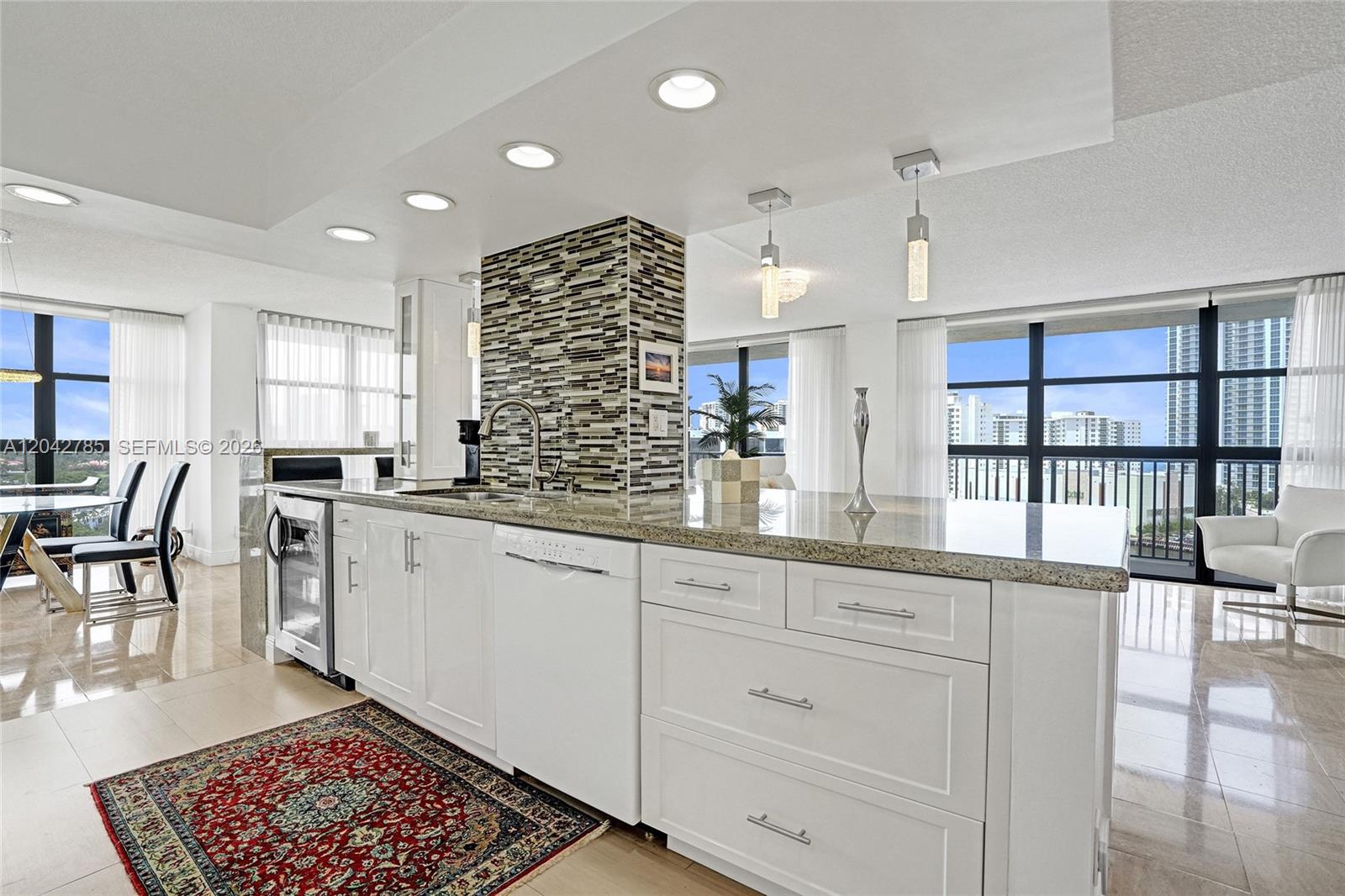 A modern kitchen features white cabinetry, granite countertops, a mosaic backsplash, and floor-to-ceiling windows — 400 Leslie Dr # 1110, Hallandale Beach FL 33009, HALLANDALE BEACH, FL