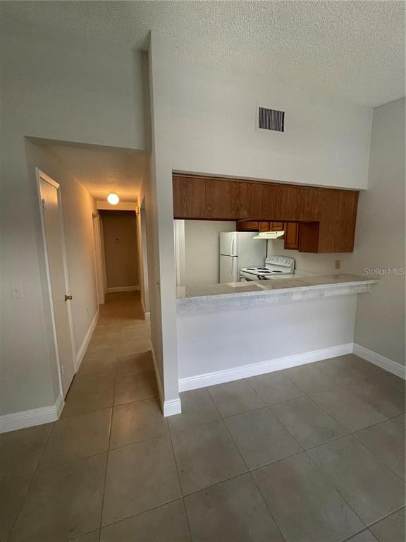 A kitchen with wood cabinets and a breakfast bar overlooks a tiled living area — 1916 CRYSTAL GROVE DRIVE, LAKELAND, FL