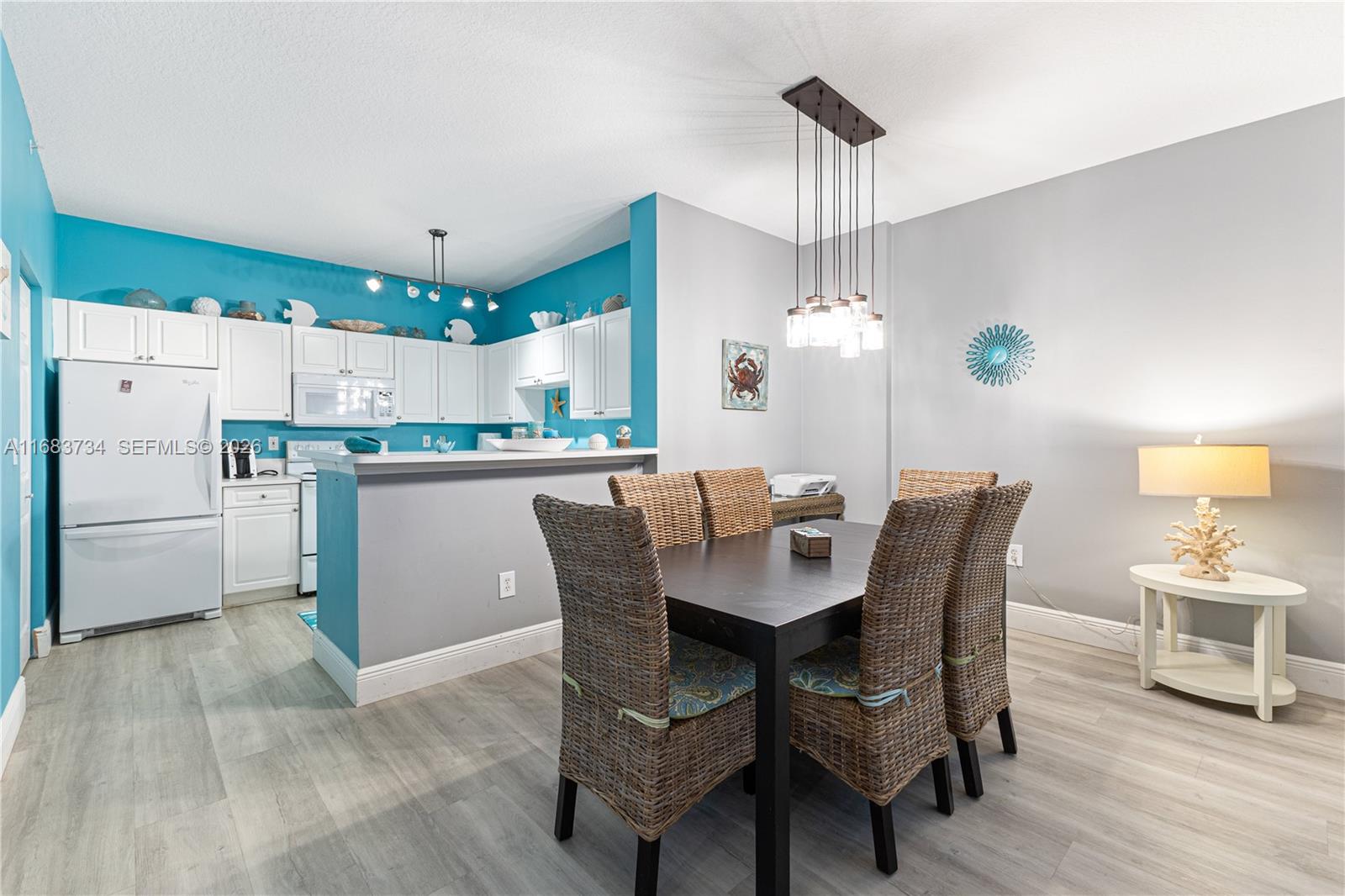 A dining area with a dark table and wicker chairs sits beside a turquoise kitchen — 651 Okeechobee Blvd # 202, West Palm Beach FL 33401, WEST PALM BEACH, FL