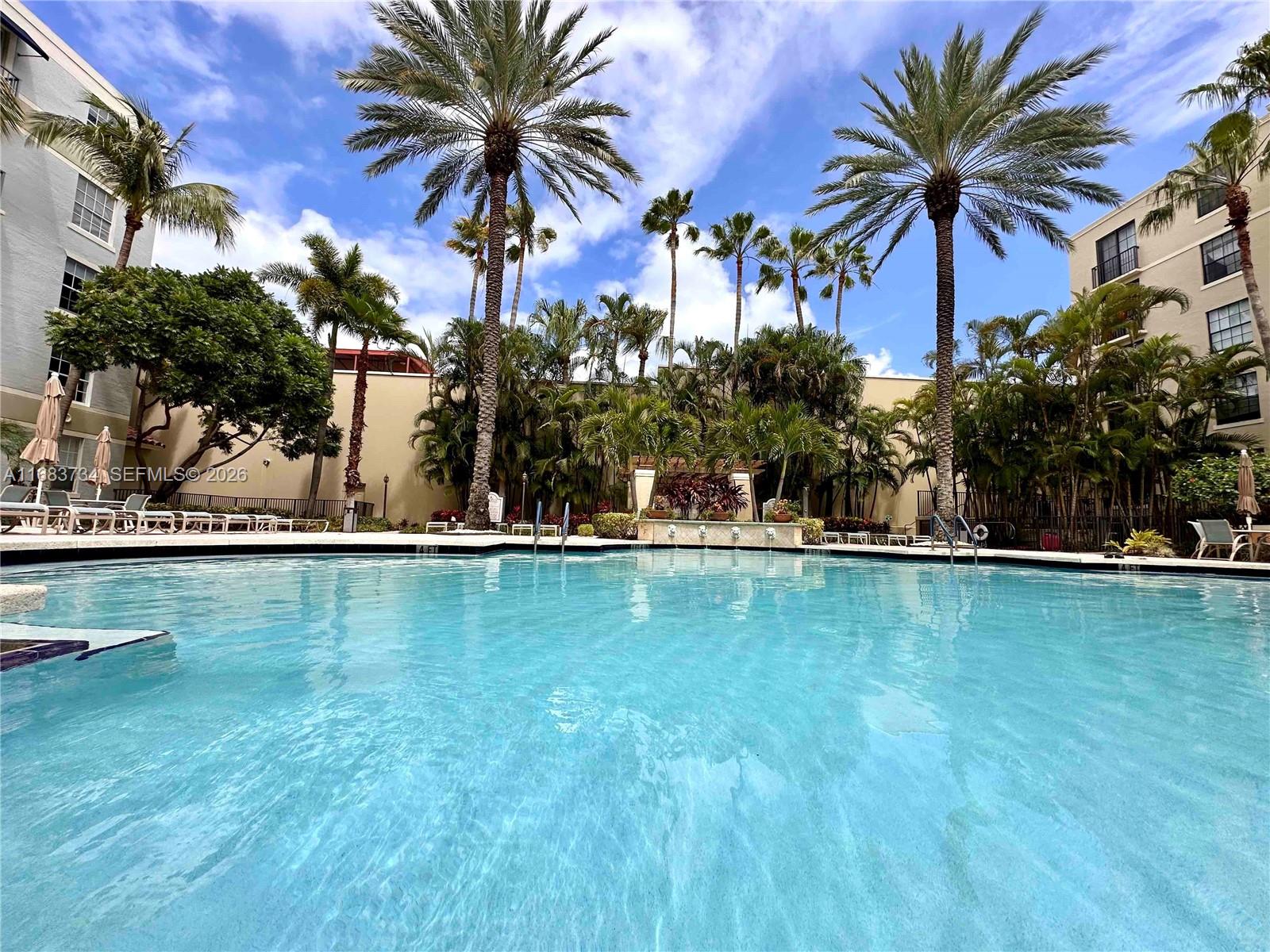 An aerial view shows a clover-shaped swimming pool surrounded by lounge chairs and palm trees — 651 Okeechobee Blvd # 202, West Palm Beach FL 33401, WEST PALM BEACH, FL