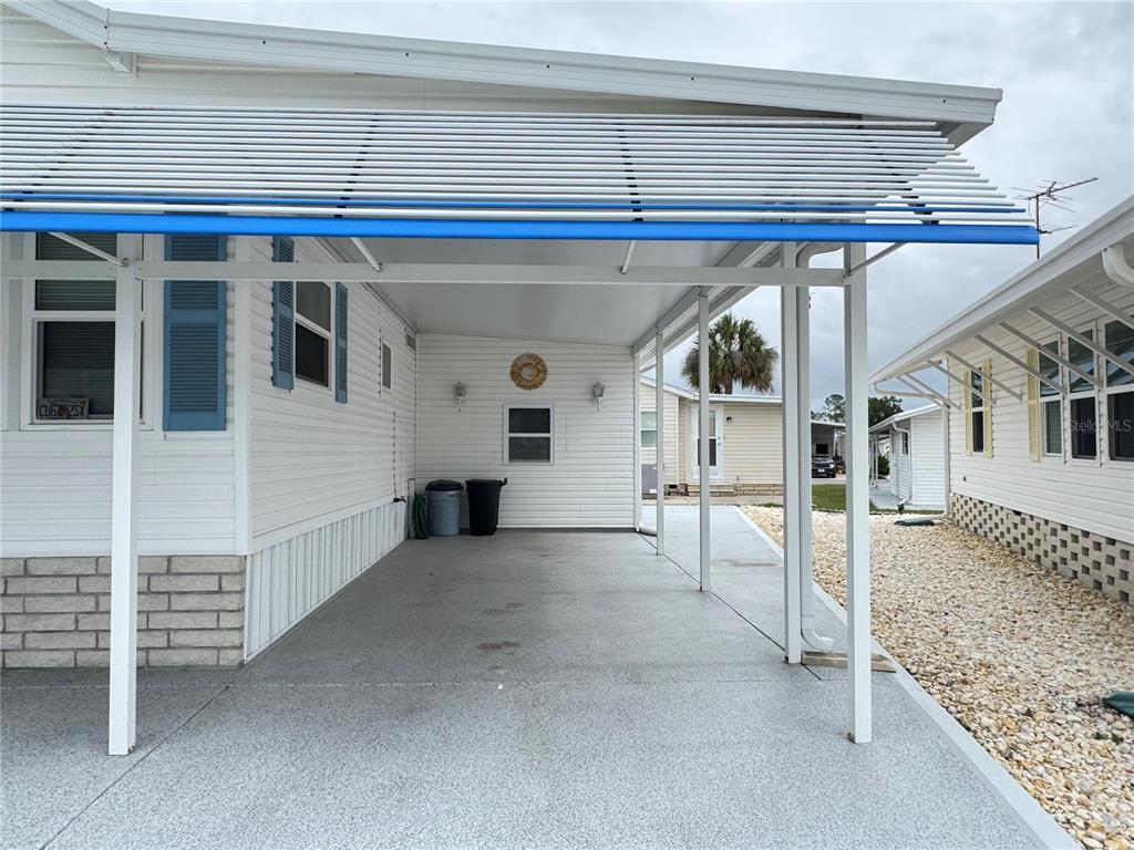 A covered carport with a concrete floor sits beside a white mobile home — 4848 BAKER AVENUE UNIT 220, ZEPHYRHILLS, FL