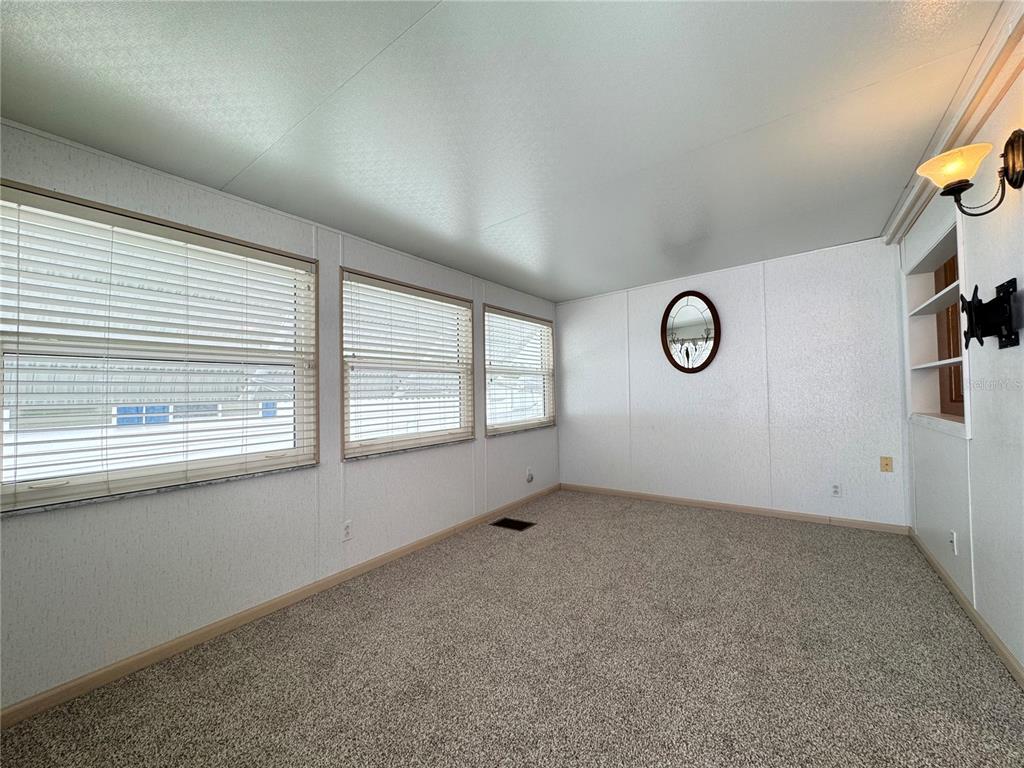 An empty room with carpeted floors, white paneled walls, and three windows with blinds — 4848 BAKER AVENUE UNIT 220, ZEPHYRHILLS, FL