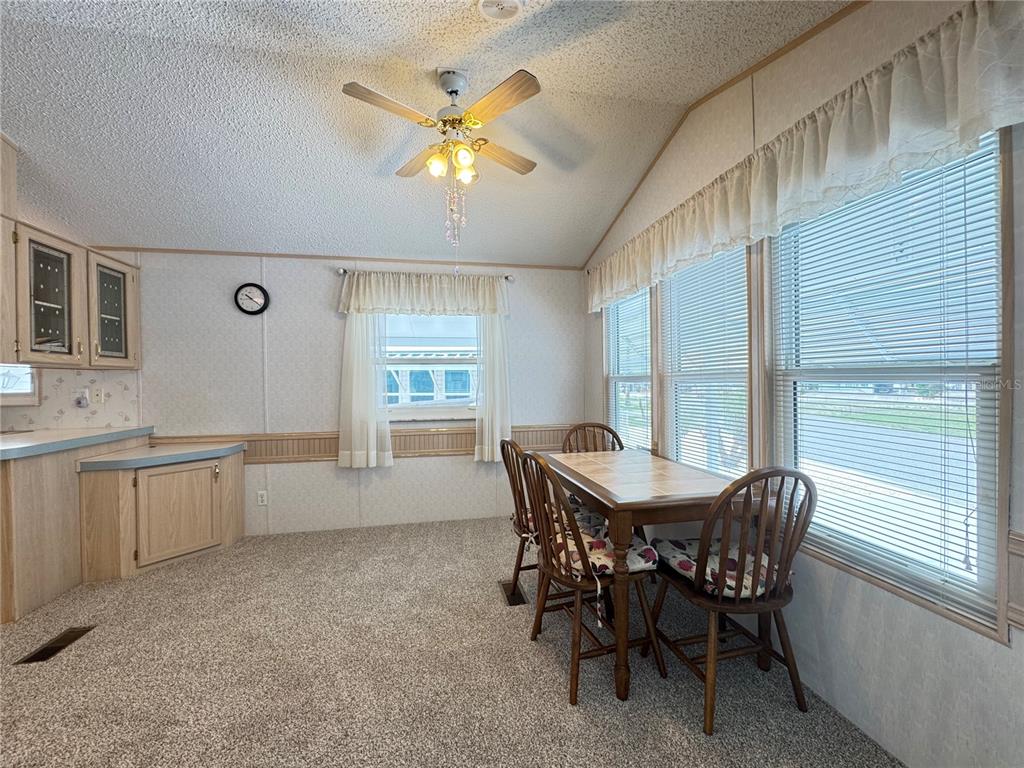 A dining area features a wooden table with four chairs, carpeted floors, and large windows — 4848 BAKER AVENUE UNIT 220, ZEPHYRHILLS, FL