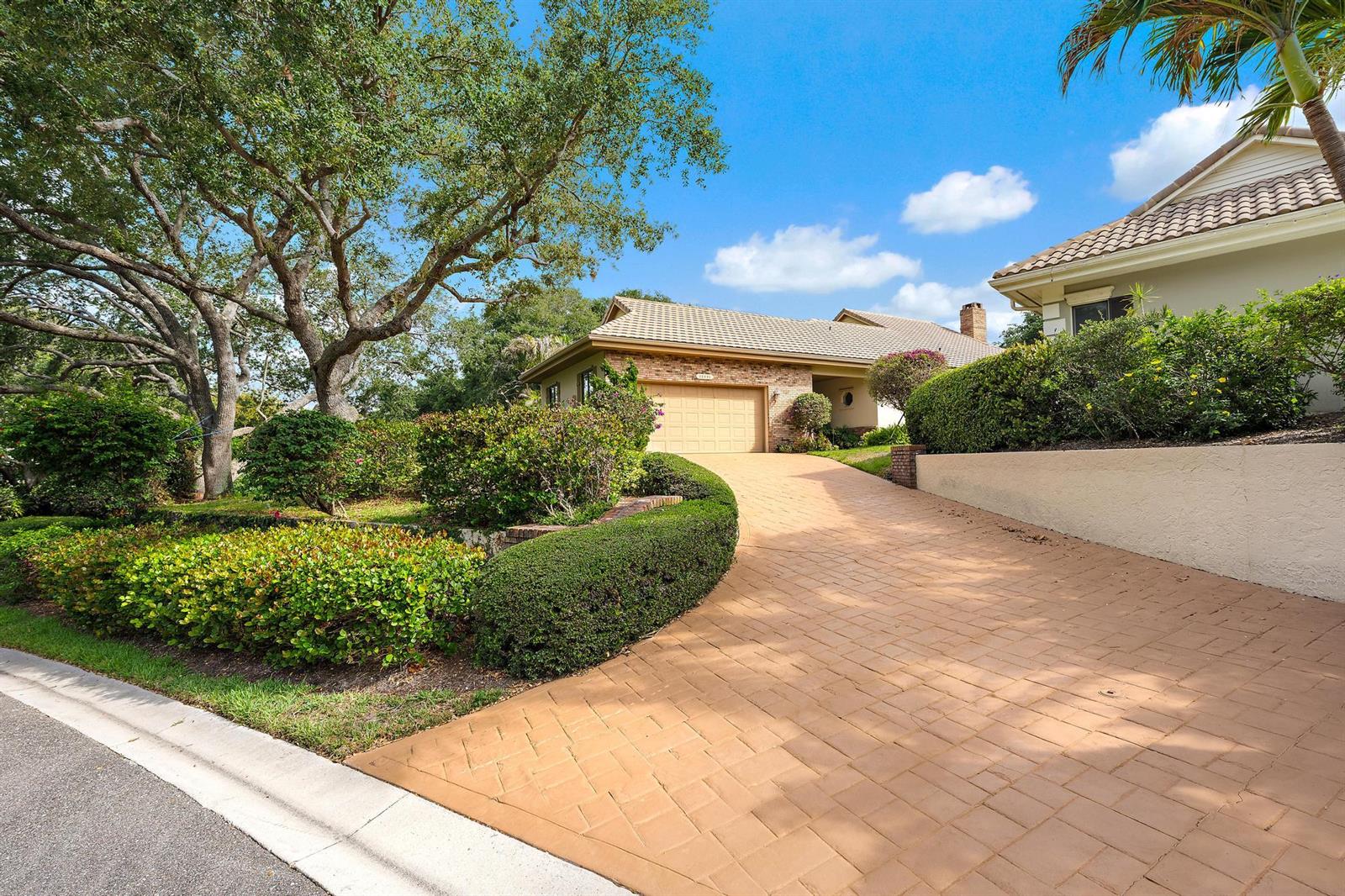 A brick house with a paved driveway and landscaped yard under a blue sky — 12001 SE Prestwick Terrace, Jupiter FL 33469, JUPITER, FL