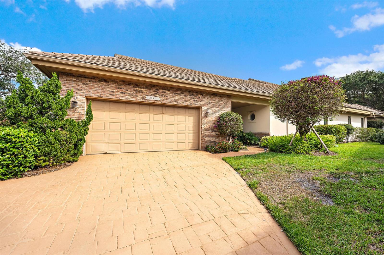 A brick house with a tan garage door and a paved driveway under a blue sky — 12001 SE Prestwick Terrace, Jupiter FL 33469, JUPITER, FL