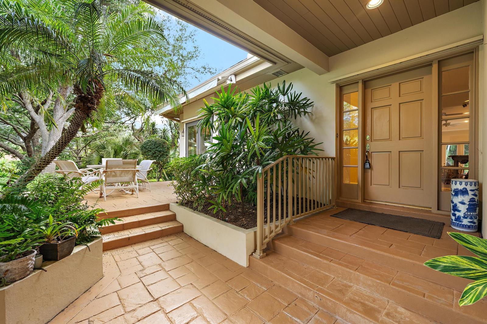 A covered patio entrance features tan tiled steps, a metal railing, and lush tropical landscaping — 12001 SE Prestwick Terrace, Jupiter FL 33469, JUPITER, FL