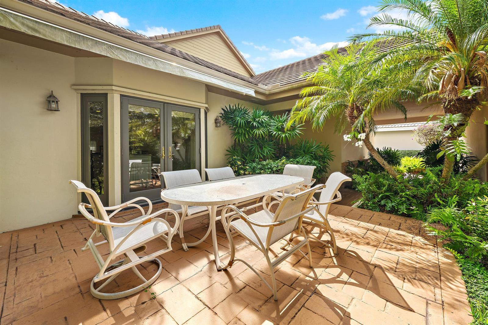 A patio features a white dining set on paved ground surrounded by lush tropical landscaping — 12001 SE Prestwick Terrace, Jupiter FL 33469, JUPITER, FL