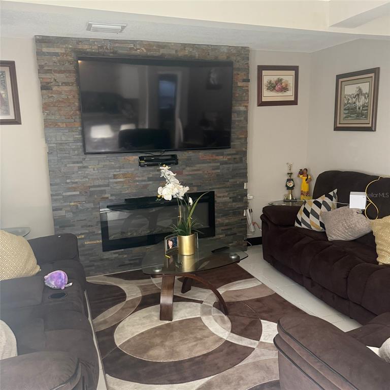 A living room features a stone-accented wall with a mounted television and electric fireplace — 10004 ETHEL STREET, GIBSONTON, FL