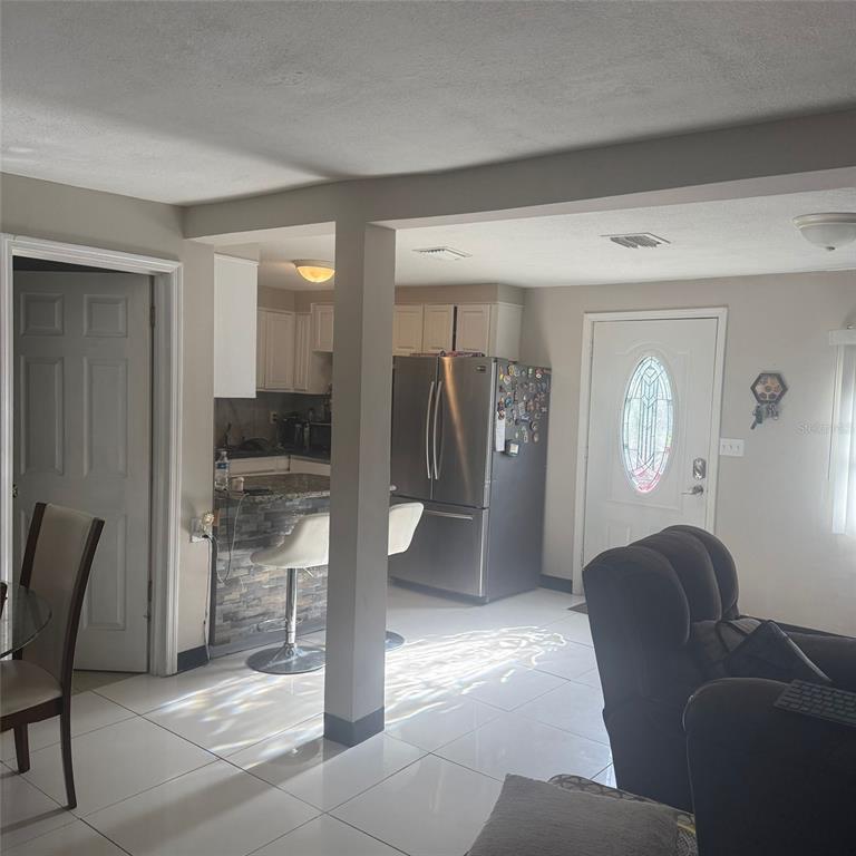 An open-concept kitchen with a breakfast bar, stainless steel refrigerator, and white tiled flooring — 10004 ETHEL STREET, GIBSONTON, FL