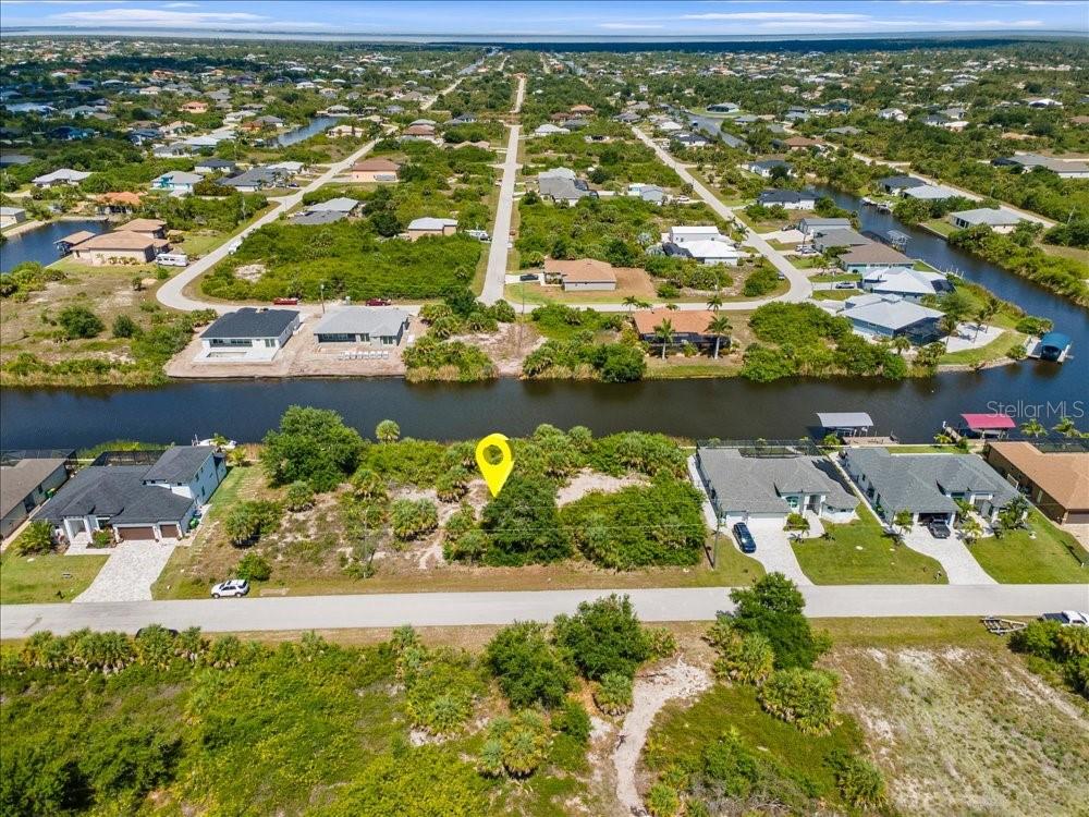 An aerial view shows a vacant, vegetated waterfront lot marked by a yellow pin — 10120 WINNIPEG STREET, PORT CHARLOTTE, FL
