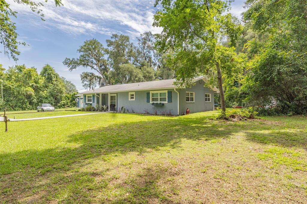 A single-story gray house with blue shutters sits on a large, grassy, tree-lined lot — 10921 COUNTY ROAD 209, OXFORD, FL