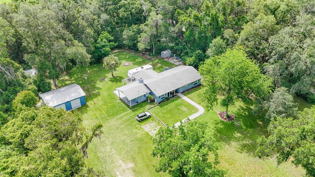 An aerial view shows a single-story house with a detached garage, camper, and wooded surroundings — 10921 COUNTY ROAD 209, OXFORD, FL