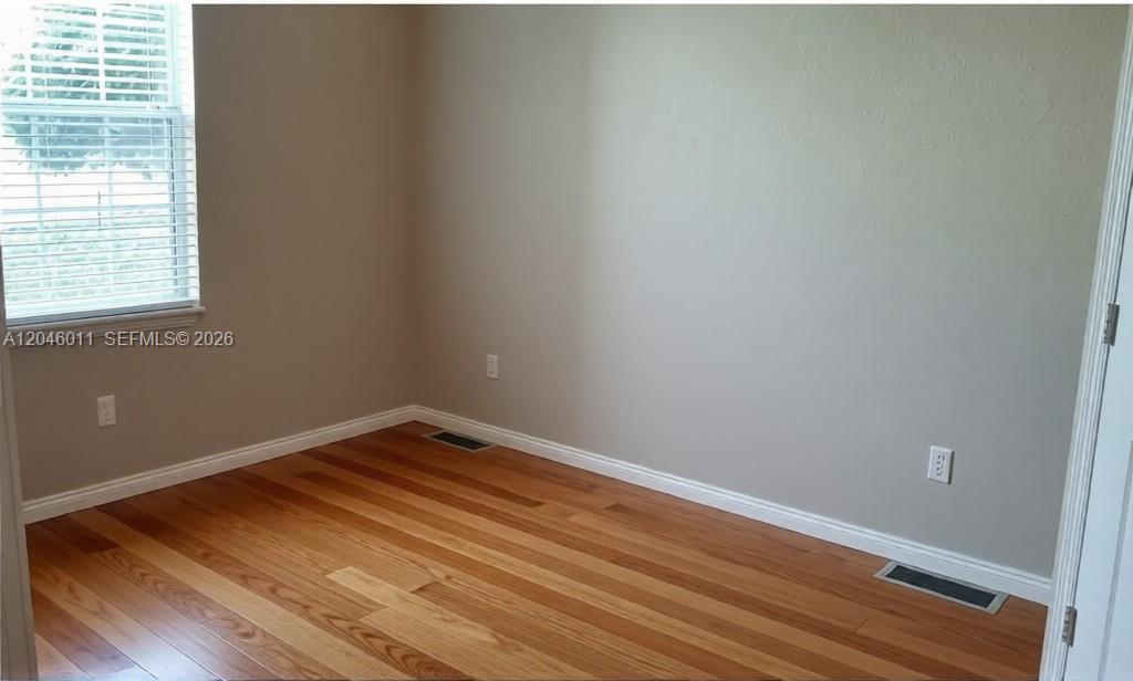 An empty room features light-colored walls, hardwood flooring, a window with blinds, and floor vents — 2788 Almaton Loop # 0, Kissimmee FL 34747, KISSIMMEE, FL